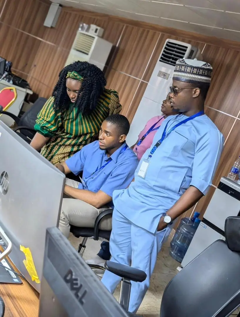 A group of professionals gathered around a desktop computer in an office workspace while reviewing information and collaborating together.